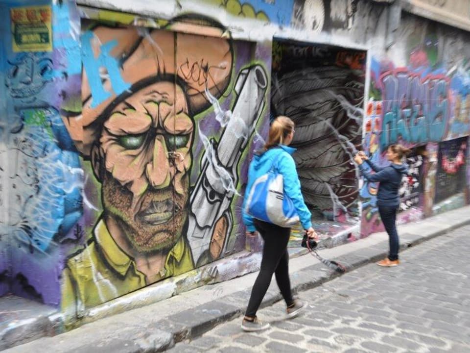 An den Hauswänden Graffitis, eine junge Frau fotografiert ein Bild.
