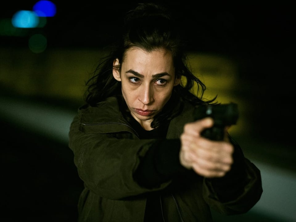 Eine Frau mit braunen Haaren zielt mit einer Waffe.