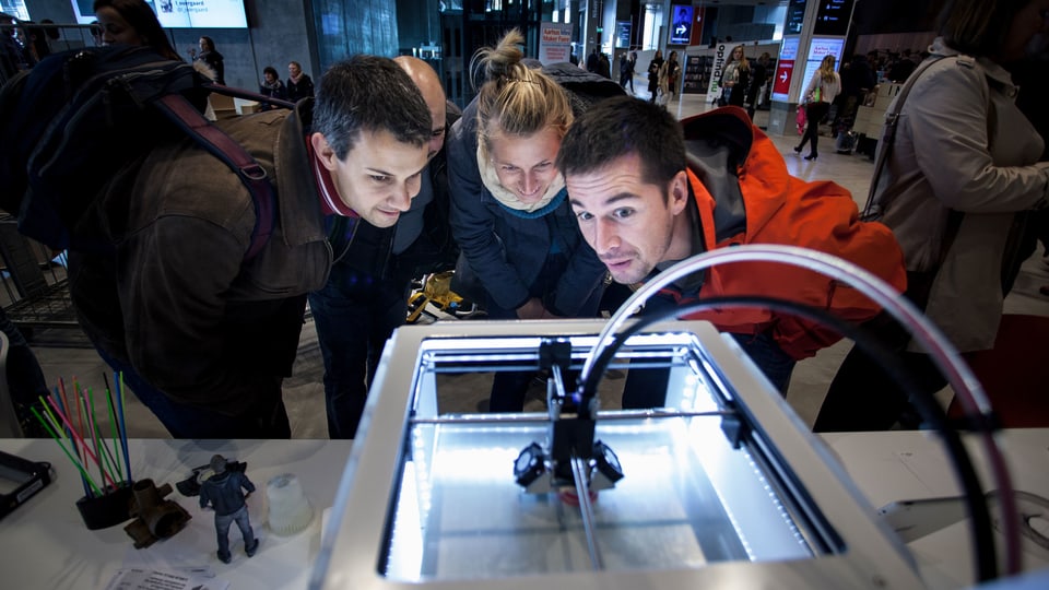 Drei Personen betrachten einen 3D-Drucker