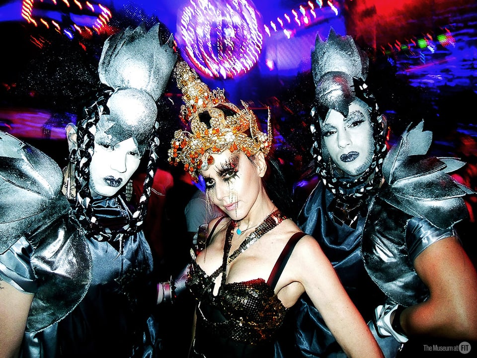 Kostümierte Frau umgeben von zwei Männers in futuristischen Kostümen.