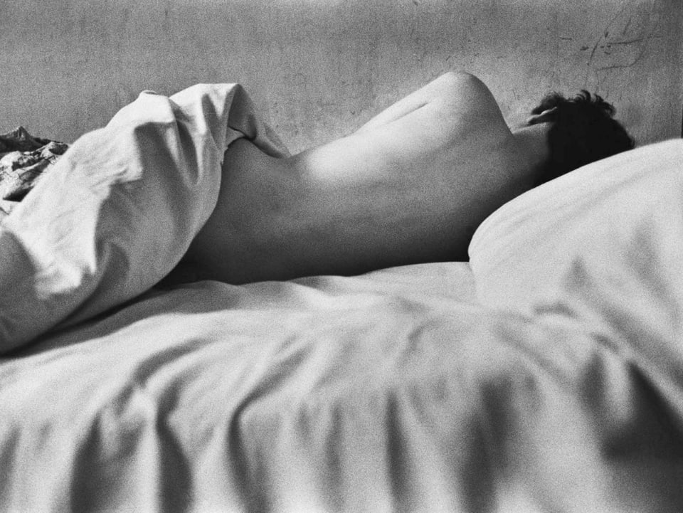 Nackte Frau auf dem Bett, dem Fotografen den Rücken zugewandt. 