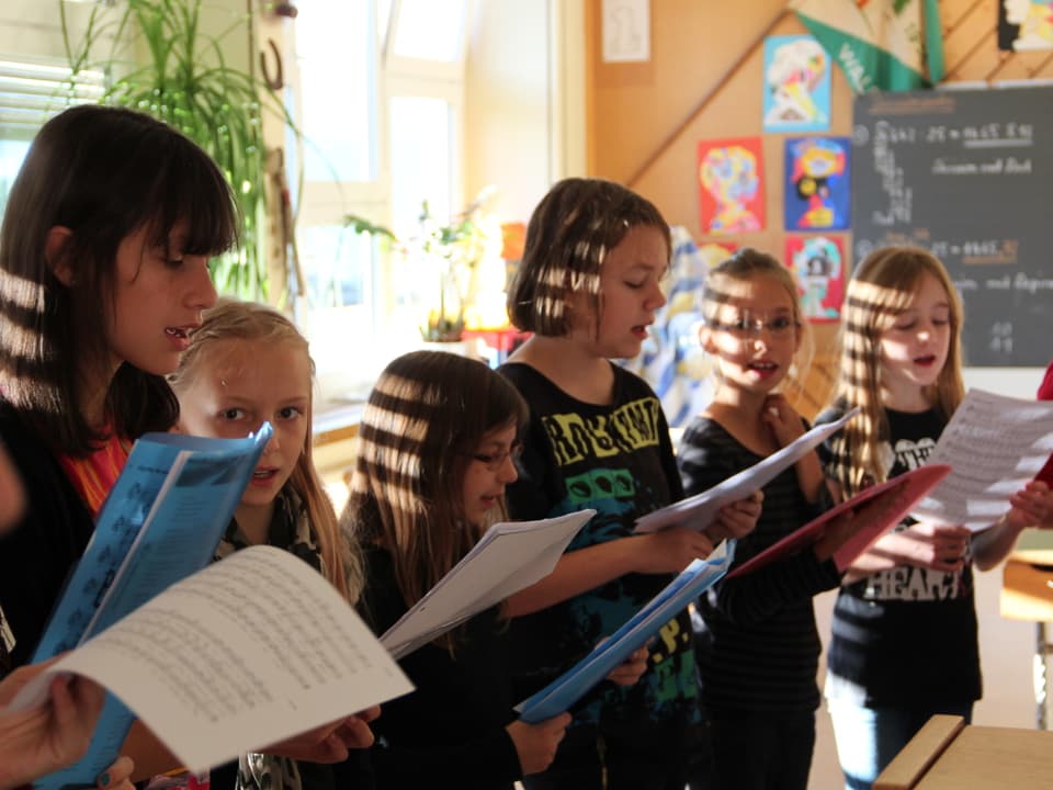 Schülerinnen mit Notenblättern, die singen.