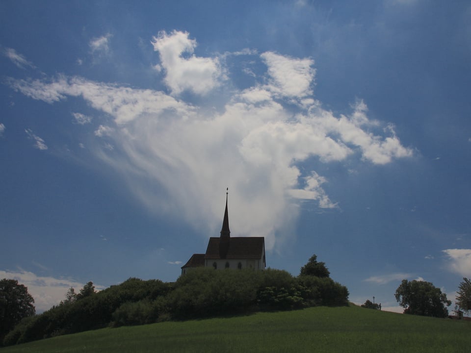 Im Vordergrund des Bildes steht eine Kirche. Hinter der Kirche sieht man eine Cumuluswolke, am unteren Ende der Wolke hängt eine Art Wolkenvorhang herunter. Den Wolkenvorhang bezeichnet man auch als Virga.