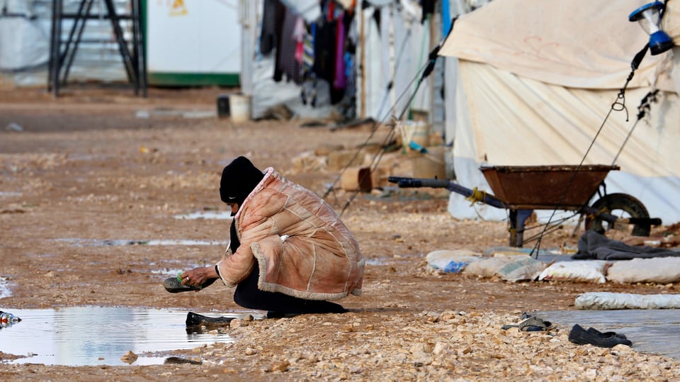 Eine Frau im Lager Zaatari wäscht ihre Schuhe in einer Pfütze. 