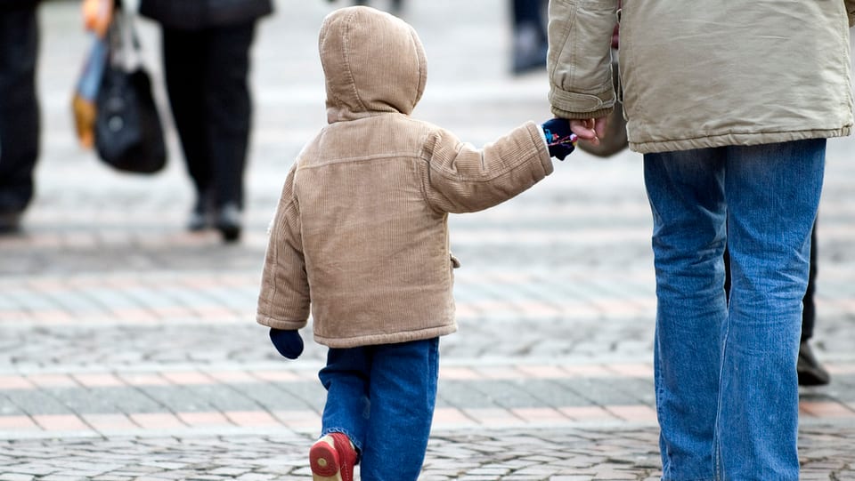 Kind mit Kapuzenjacke an der Hand eines Erwachsenen.