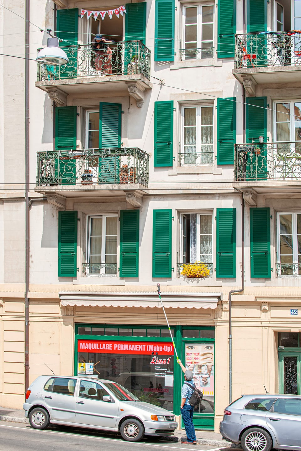 Ein Mann steht auf einer Strasse und streckt ein Teleskop-Mikrophon in Richtung einer Frau auf einem Balkon im zweiten Stock.