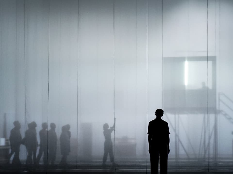 Theaterszene: Menschen auf einer Bühne im Nebel.