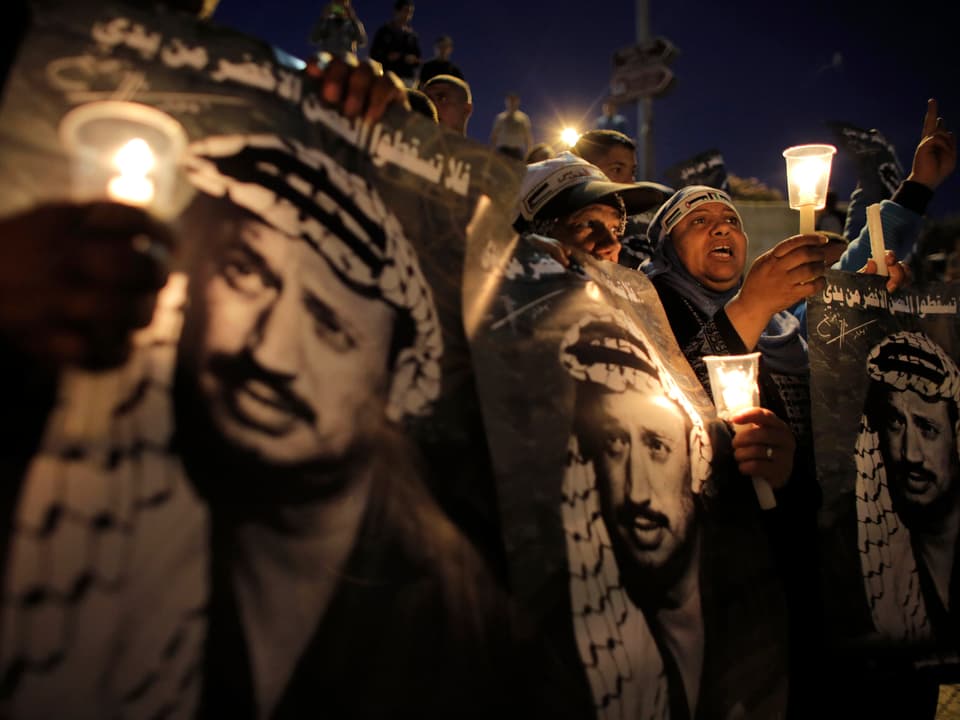 Menschen halten Porträts von Jassir Arafat und Kerzen in den Händen.