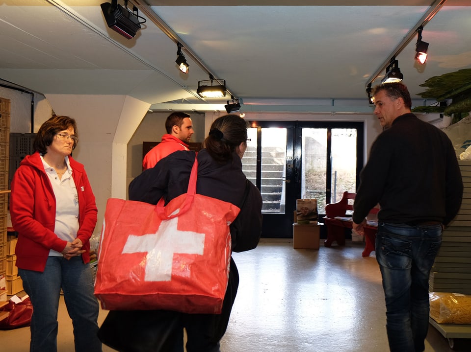 Eine Frau trägt eine Tasche mit einem aufgedruckten Schweizerkreuz und spricht mit drei Menschen.
