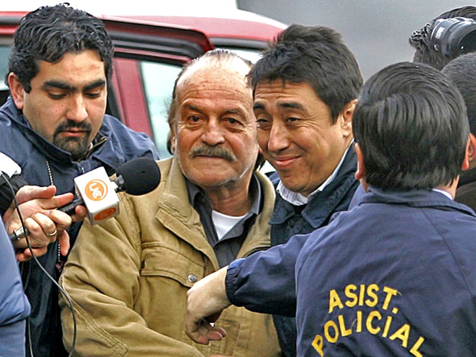 2007: Ex-General Raul Iturriaga ist in Santiago, Chile, von Polizisten umringt. Ein Journalist hält ihm ein Mikrophon vor den Mund.