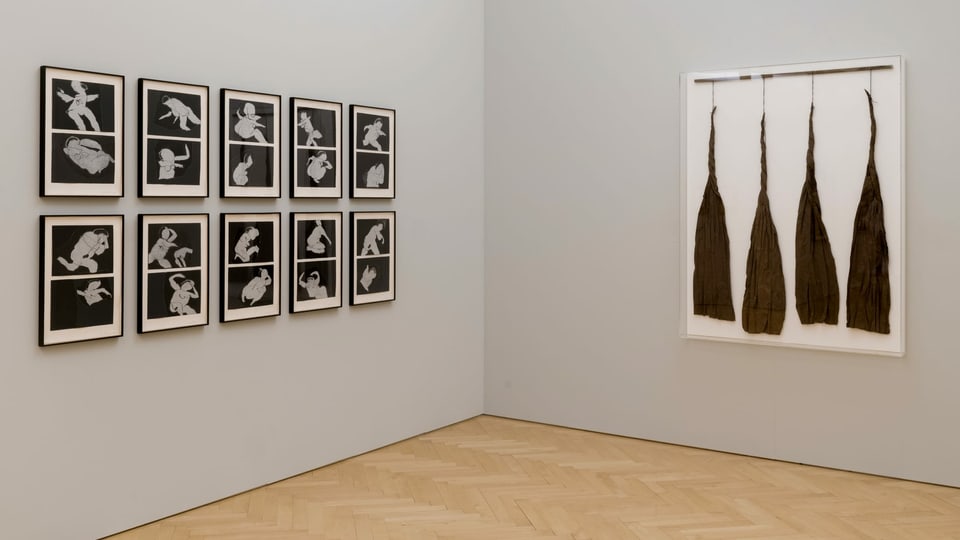 10 Schwarz-Weiss-Bilder mit abstrakten Frauenfiguren hängen an einer grauen Wand.