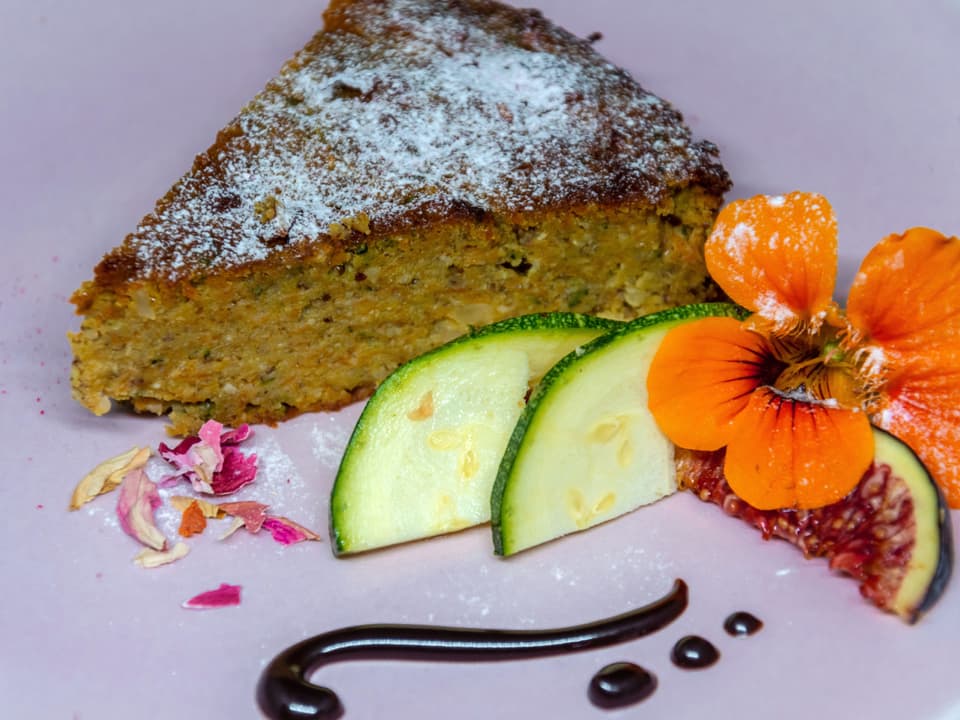 Ein Kuchenstück auf dem Teller, garniert mit Blume und Feige.