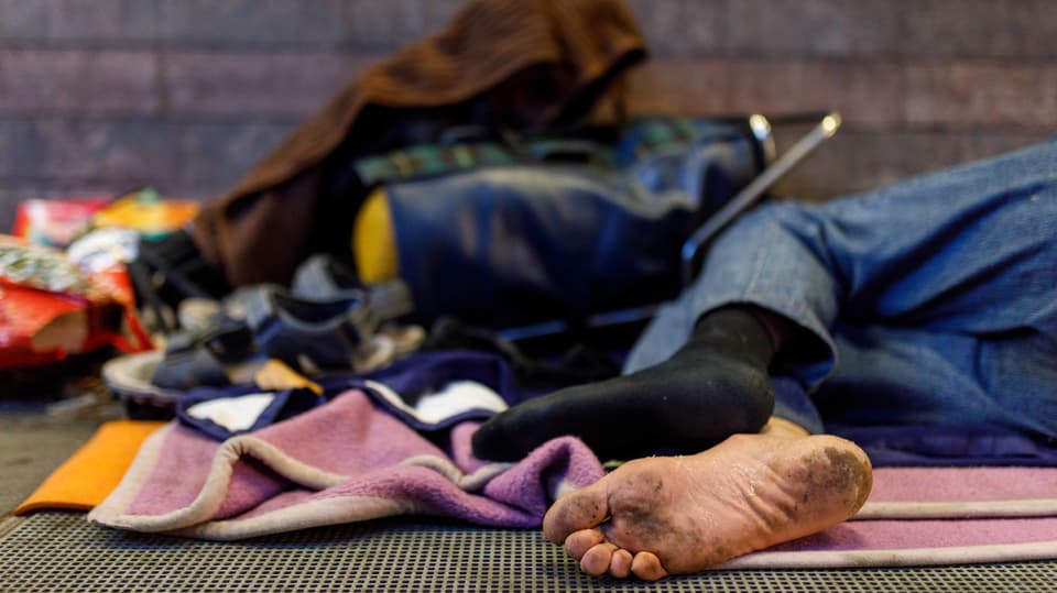Obdachloser liegt mit Kleidern am Boden in einer Stadt