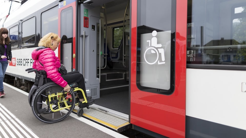 Eine Frau im Rollstuhl rollt in einen SBB Zug. 