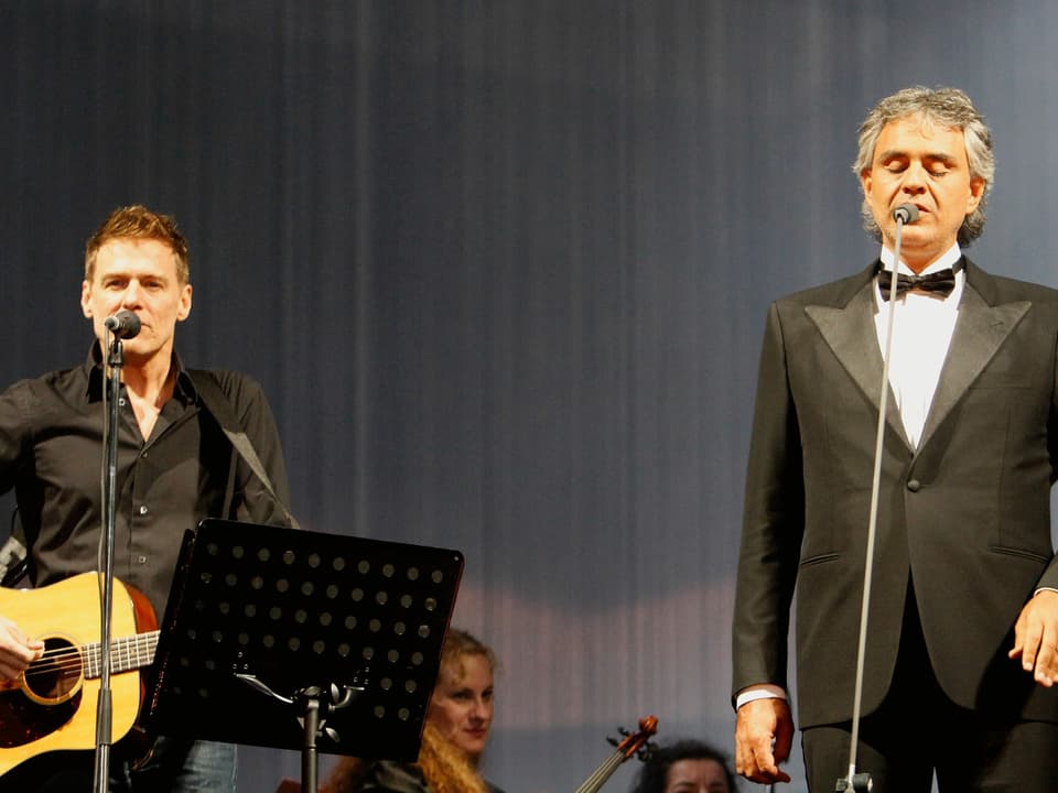 Bryan Adams steht mit Andrea Bocelli auf der Bühne.