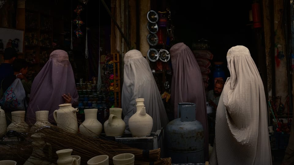 vier verschleierte Frauen, in Burka, stehen um Tonkrüge.
