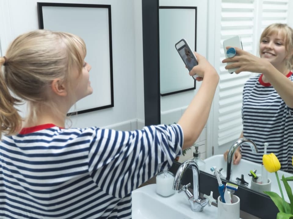 Frau fotografiert sich im Badezimmerspiegel.