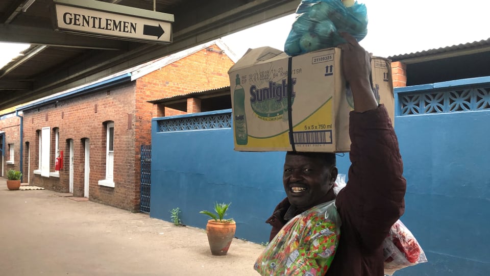 Ein Mann beladen mit Kartonschachteln und Taschen im Bahnhof von Bulawayo.