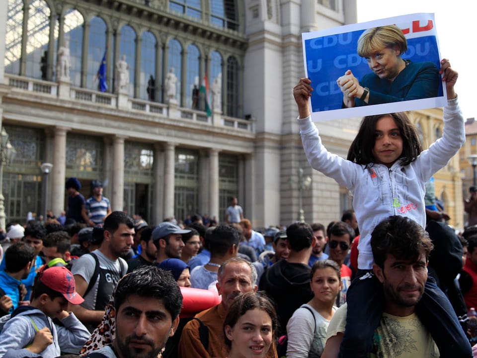 Ein Flüchtlingsmädchen streckt ein Bild von Angela Merkel in die Höhe. 