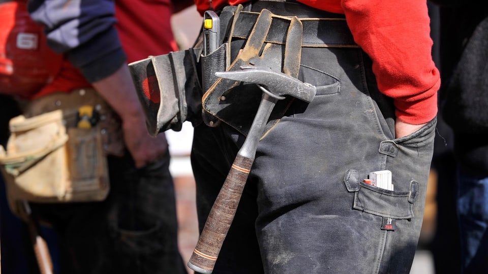 Hüfte eines Bauarbeiters mit einem umgebundenen Werkzeuggürtel, daran baumelt ein Hammer.