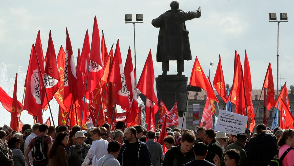 Demonstranten und rote Fahnen um eine Lenin-Statue.