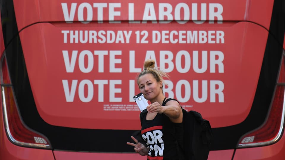 Eine Frau macht ein Selfie vor einer Labour-Werbung