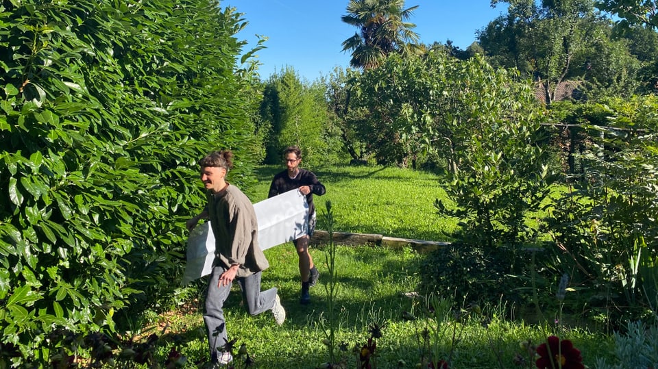 Eine junge Frau und ein junger Mann halten ein Banner in der Hand und rennen durch einen Garten.