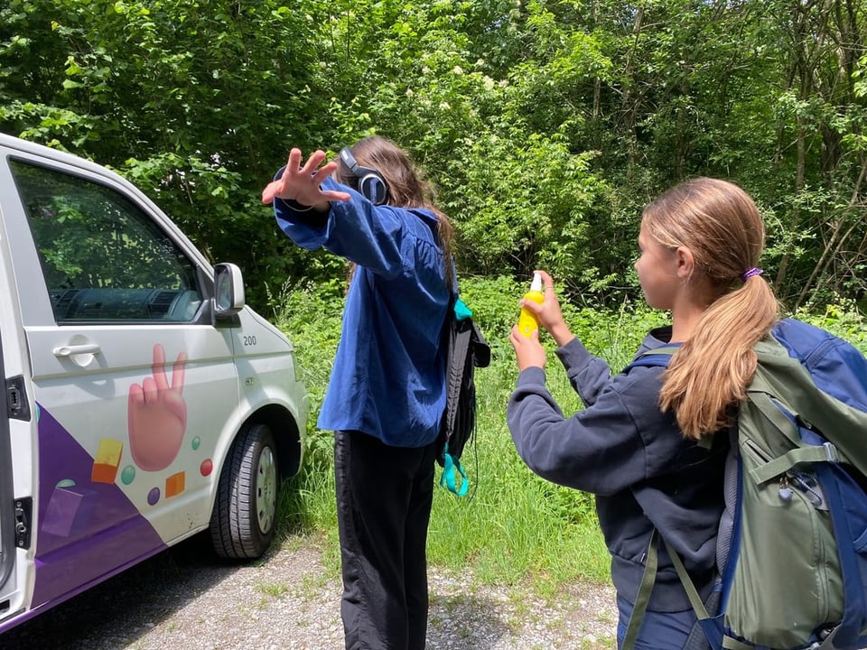 Ein Mädchen sprayt eine Frau im Wald mit Zeckenspray ein. 