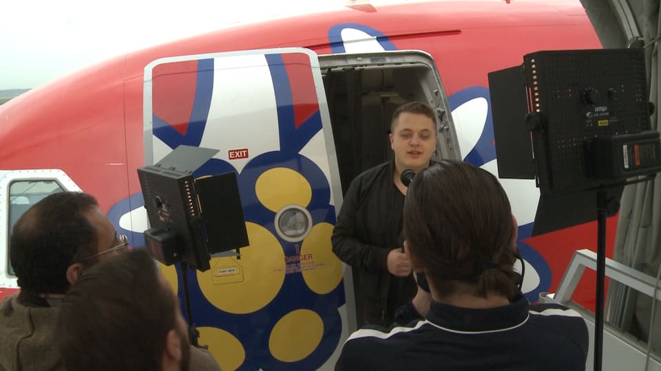 Ein junger Mann steht im Eingang eines Flugzeugs, er ist umgeben von Fernsehkameras.