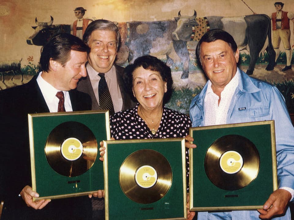 Zwei Männer und eine Frau zeigen lachend ihre Goldene Schallplatte.