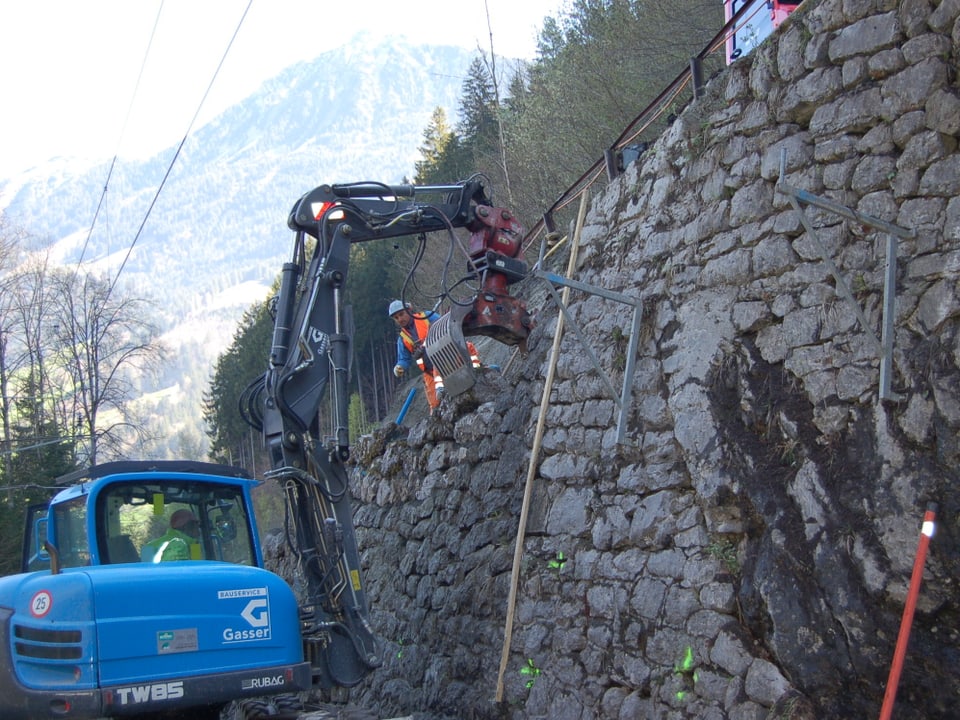 Arbeiter mit Bagger sanieren eine Natursteinmauer.