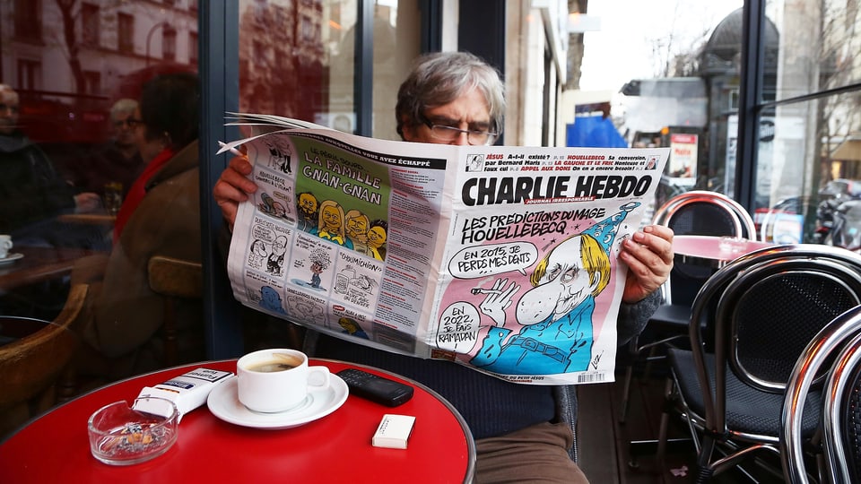 Ein Mann in einem Café liest die Zeitung "Charlie Hebdo".
