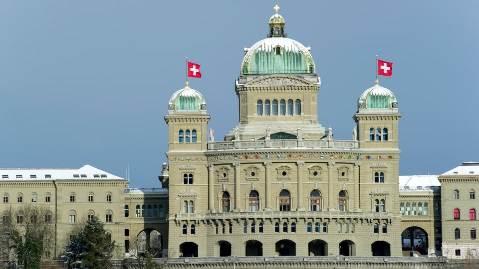Das Bundeshaus mit wehenden Schweizer Fahnen und schneebedeckten Kuppeln.