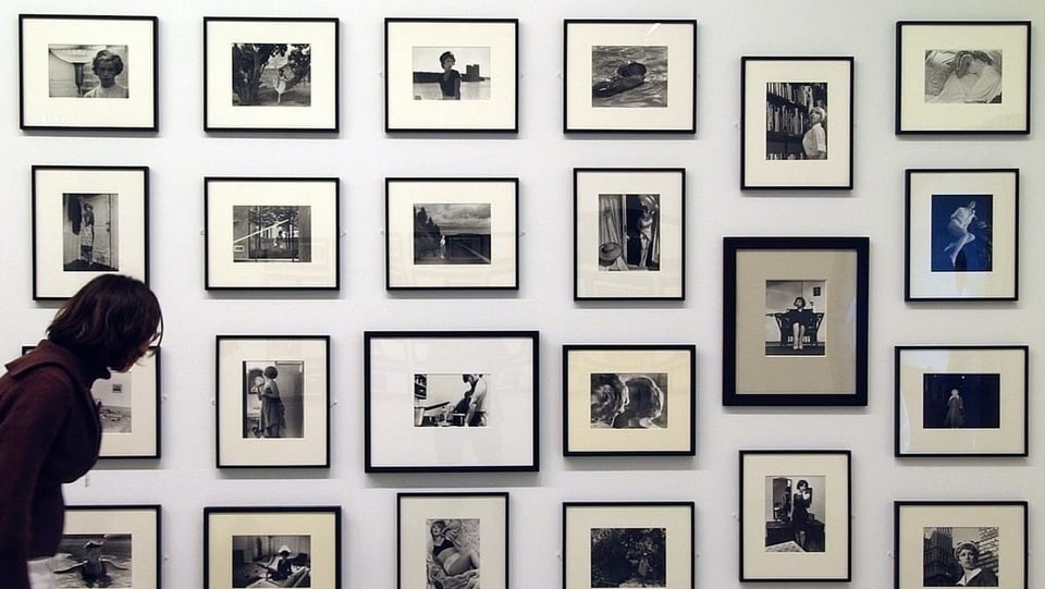 Eine Frau schaut sich im Museum ein Foto an, das mit vielen anderen Bildern an einer Wand hängt.