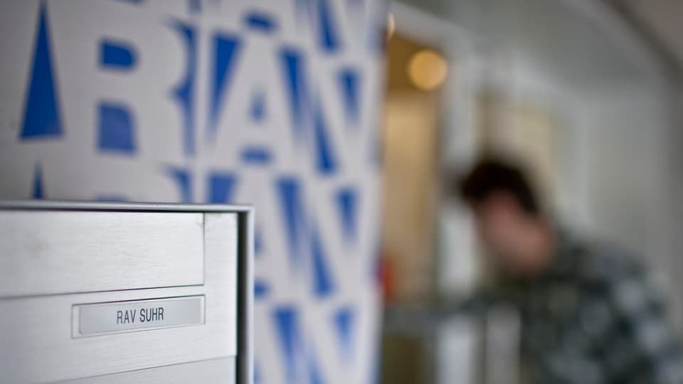 Der Briefkasten des RAV in Suhr, im Hintergrund das Logo an der Wand und ein Mensch, der das Büro betritt.