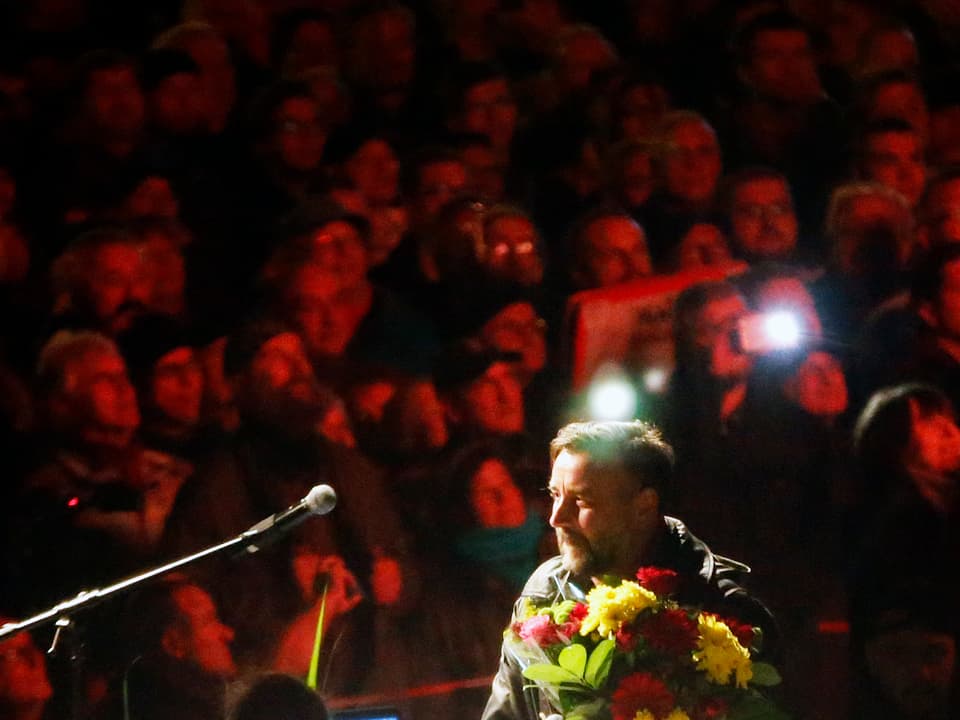 Pegida-Gründer Lutz Bachmann mit einem Blumenstrauss in der Hand, hinter ihm die Demonstranten. 