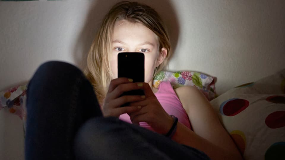 Symbolbild: Mädchen sitzt auf ihrem Bett und surft mit dem Handy.