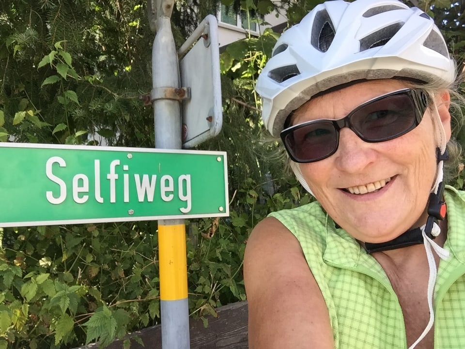 Eine posiert neben einem Strassenschild, auf dem steht: Selfiweg.