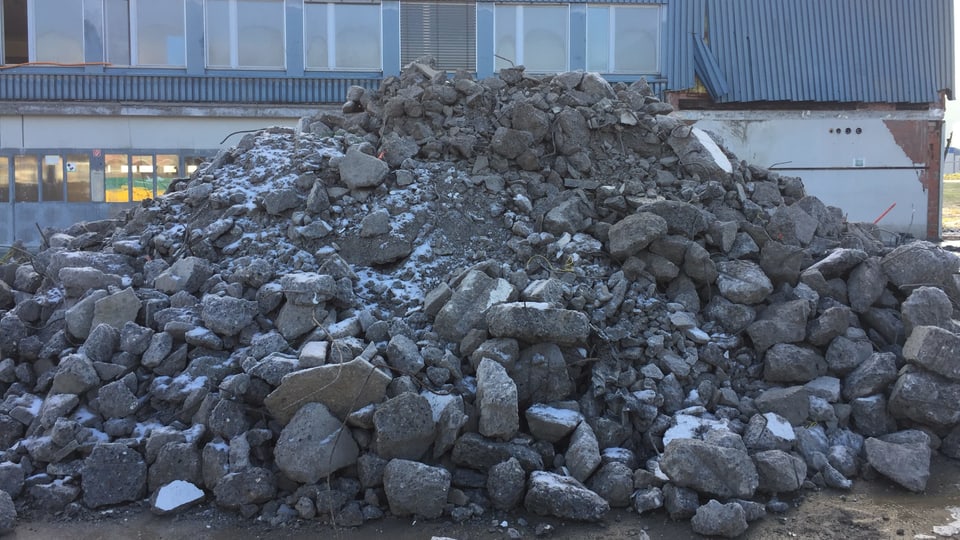Ein Haufen grosser Steine liegt auf einem Platz vor einer Lagerhalle. 