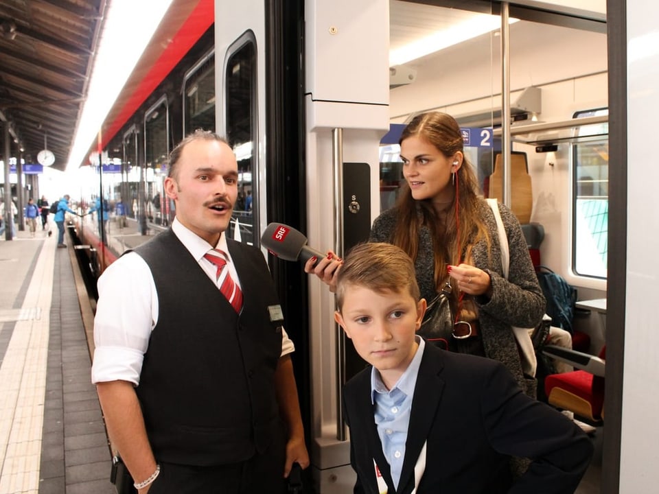 Zugbegleiter Arno, Moderatorin Angela und Kinderreporter Noel vor dem Zug