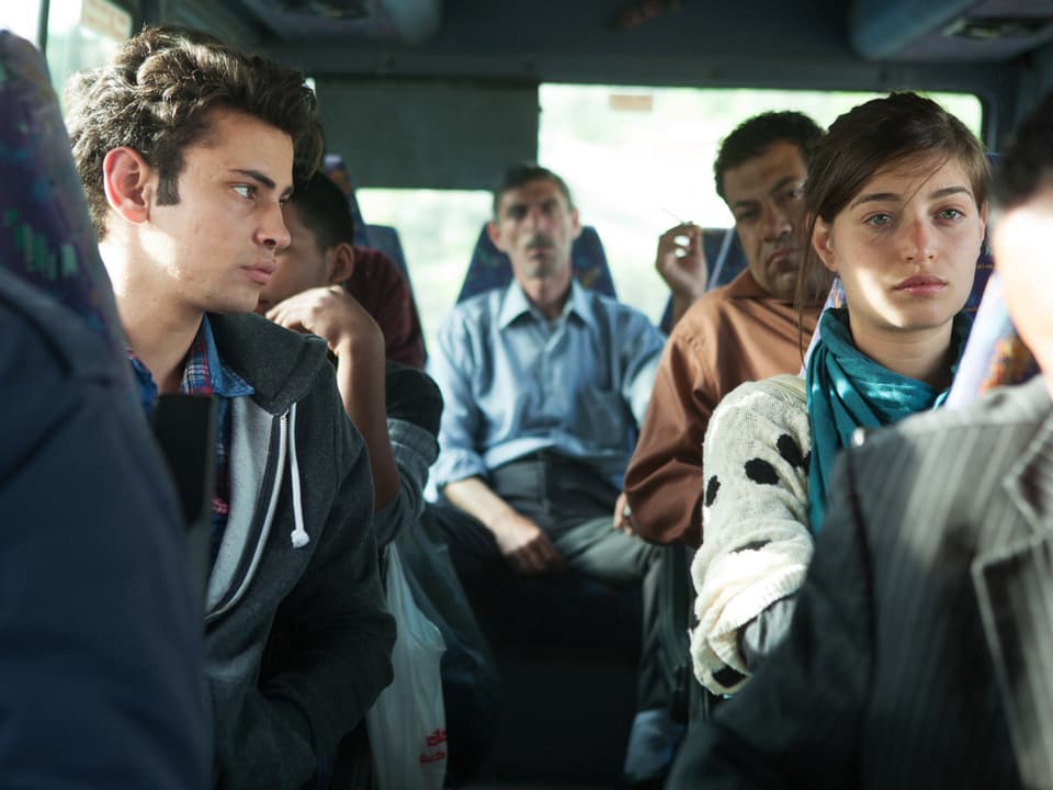 Ein junge schaut in einem Bus zu einem Mädchen rüber.