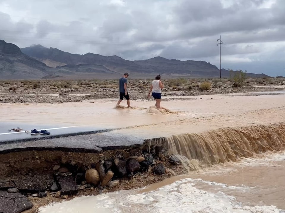 Zwei Menschen waten durch eine überflutete Strasse im Death Valley.