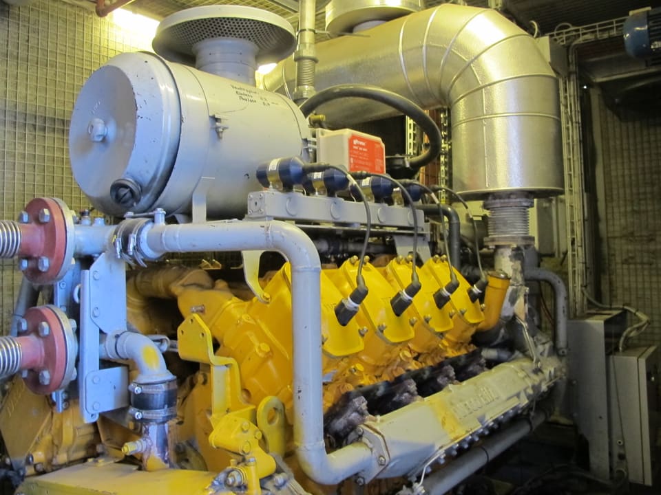 Ein grosser gelber Motor ist zu sehen, zusammen mit vielen Röhren und Kabeln.