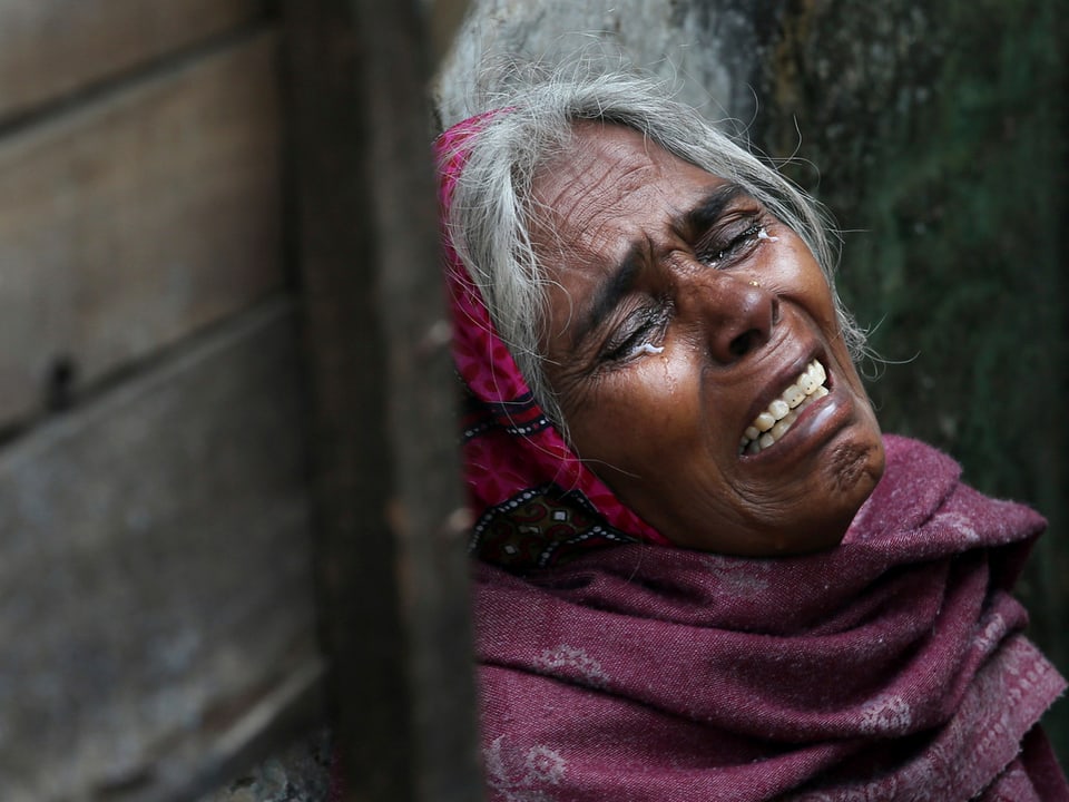 Eine Inderin mittleren Alters lehnt sich an eine Wand und weint.