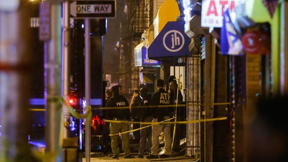 Polizisten mit Schutzwesten stehen nachts vor Geschäften in einer Strasse von Jersey City. Gelbe Bänder sichern den Tatort.