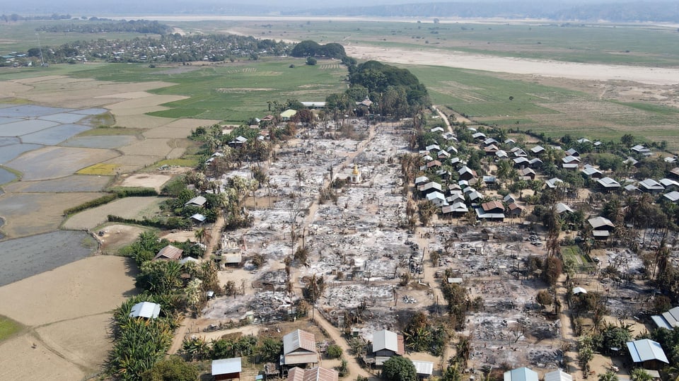 Blick von oben auf ein Dorf, umgeben von Feldern,  in dem rund die Hälfte der Häuser zerstört ist