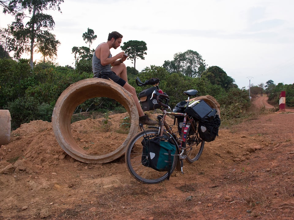 Lukas Biry sitzt auf einer grossen BEtonröhre und macht Pause, das Fahrrad steht vor der Röhre.