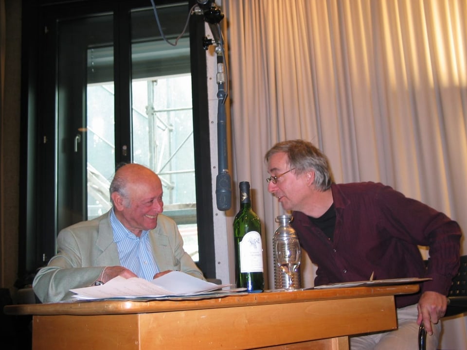 Patrick Elias und Ueli Jäggi sitzen am Tisch mit einem Mikrofon. 