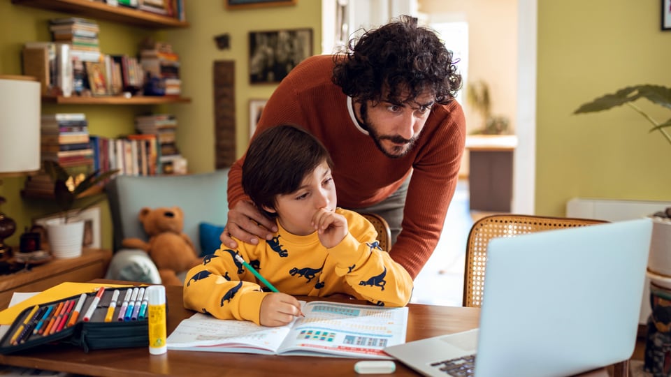 Ein Vater hilft seinem Sohn bei den Hausaufgaben vor dem Laptop.