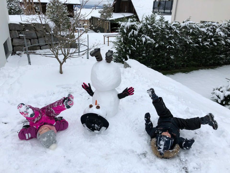 Ein Schneemann und zwei Kinder strecken die Füsse in die Luft.